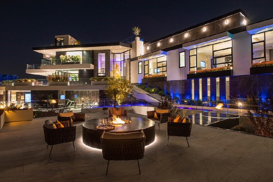 well-lit luxury home in the evening with colorful lighting and a firepit in the foreground. 