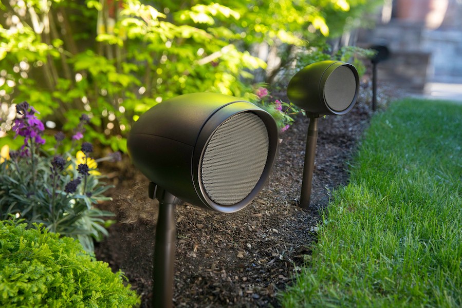 Triad outdoor speakers installed among the mulch around a plant