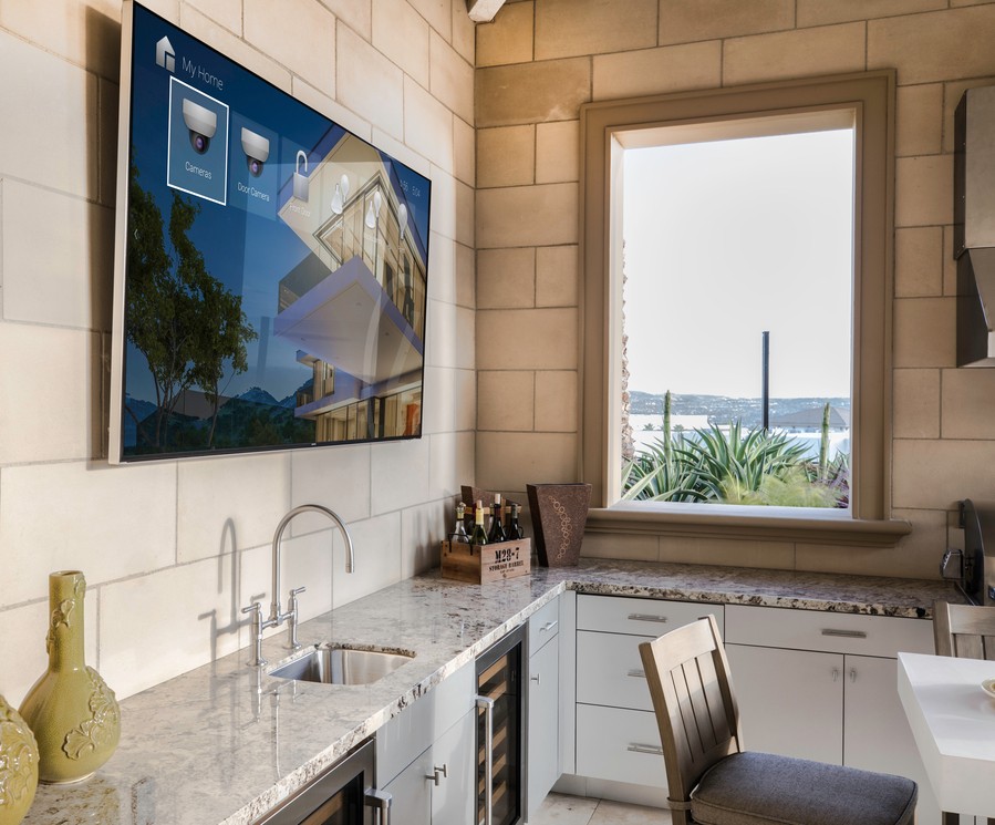 kitchen counter sink with a wall-mounted TV above it showing a Control4 interface