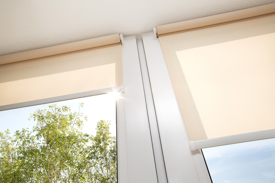 Image is of a pair of off-white motorized shades pulled down over the windows in a home.
