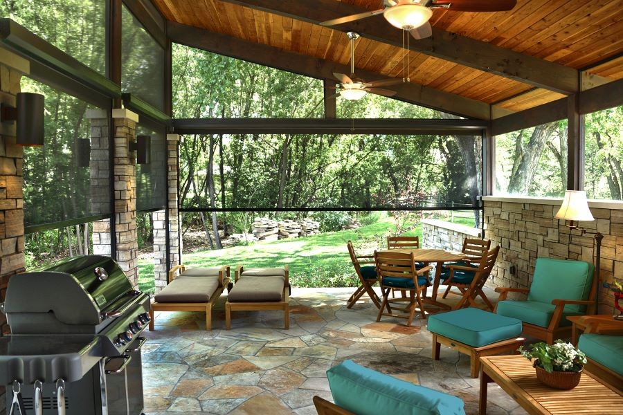 An outdoor patio with a grill, seating areas, and lighting enclosed by halfway lowered motorized outdoor shades.