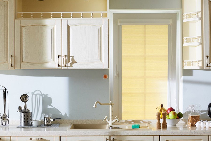 A kitchen countertop with a window that has lowered yellow blinds.